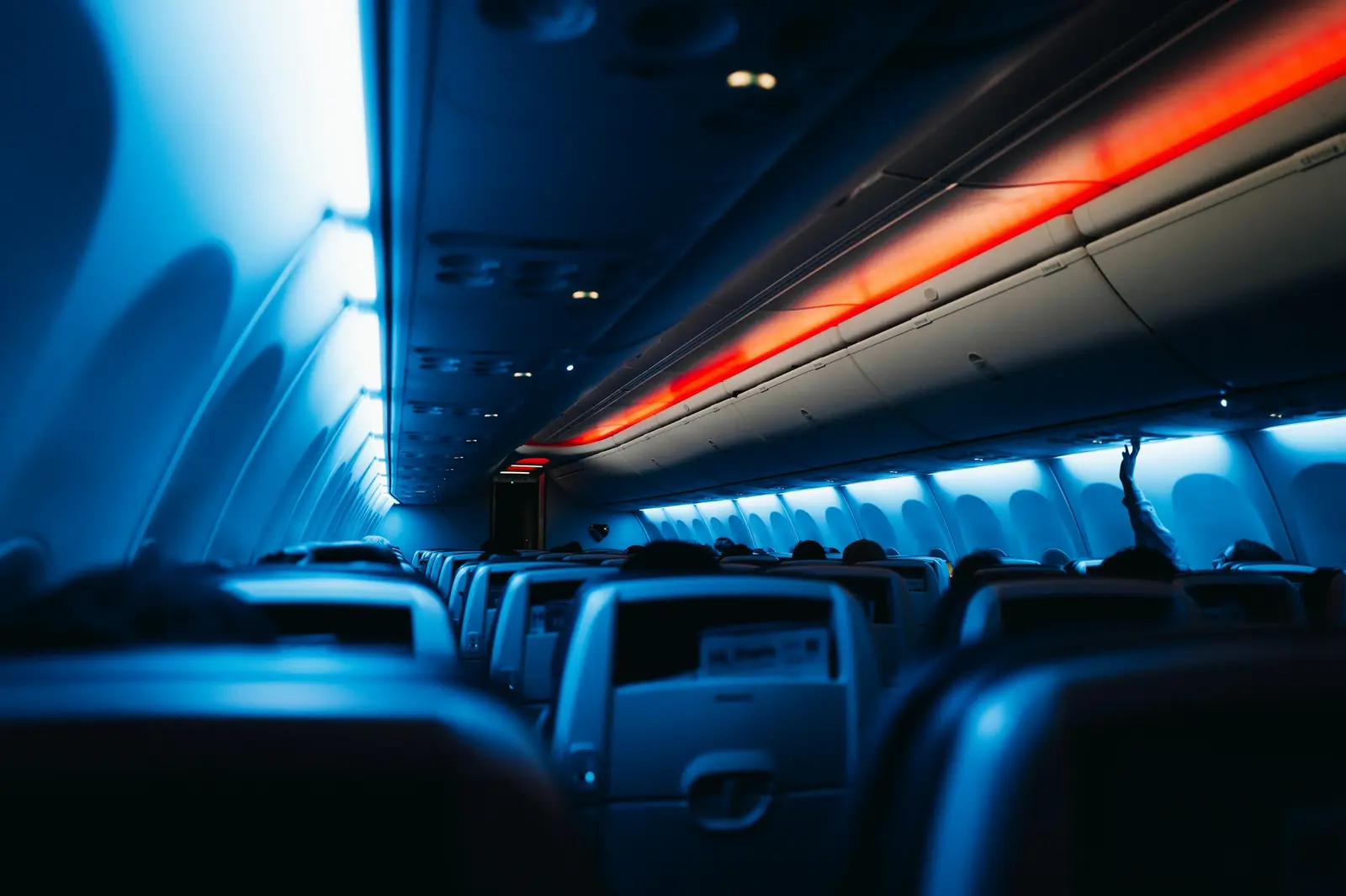 Moody blue and red mood lighting inside an airplane cabin during a night flight, rows of headrests visible