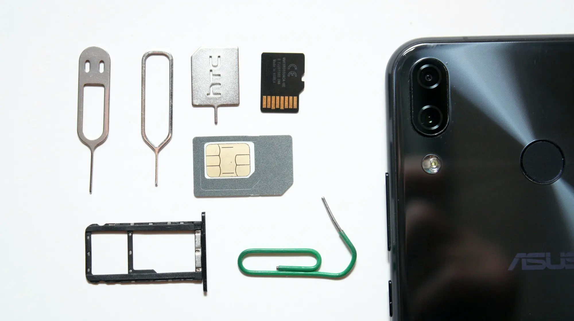 A physical nano-SIM card, SIM tray, and ejector tools laid out next to a smartphone